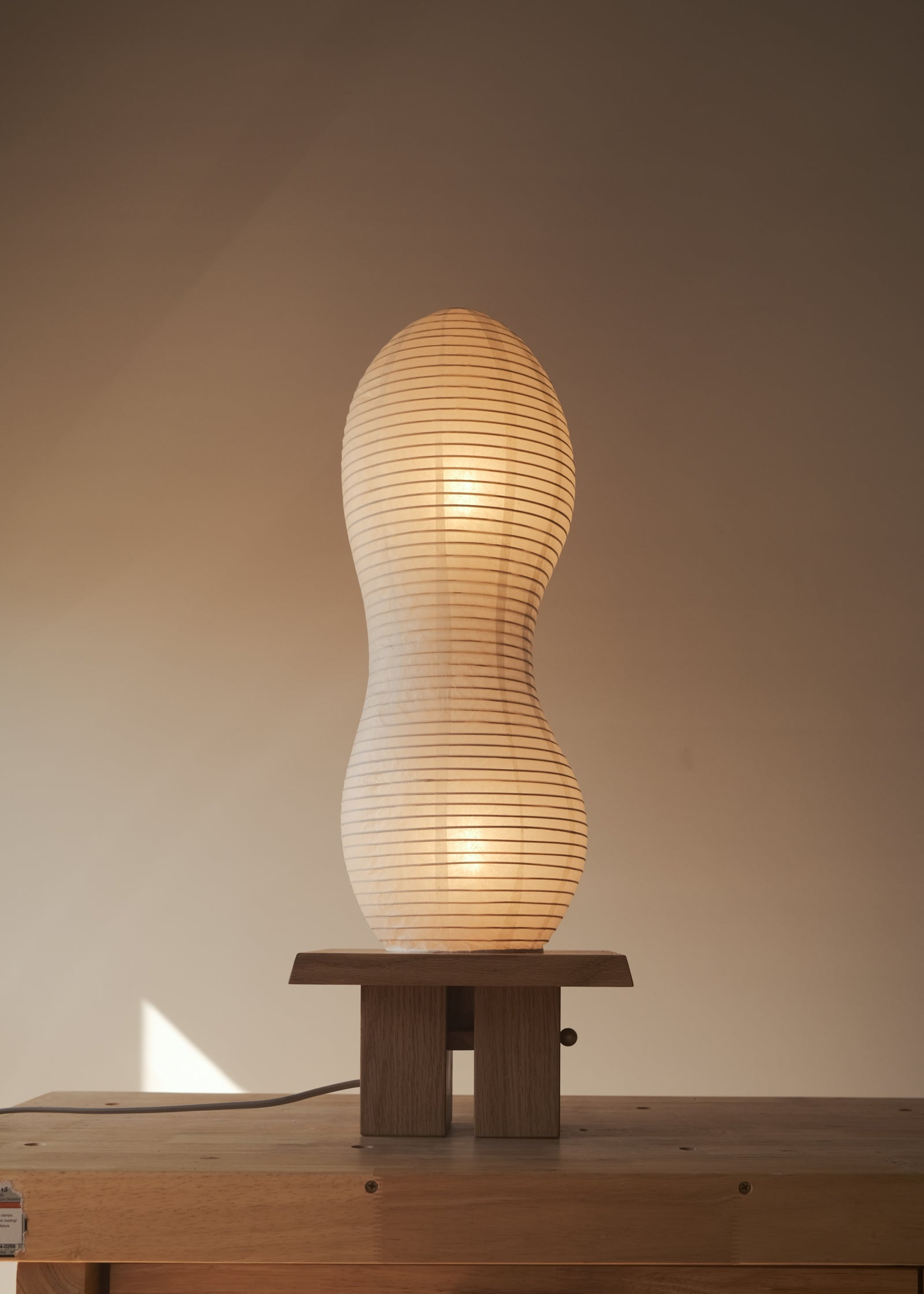 A straight-on shot of Kawabi's Legume Lamp made of Japanese washi and White Oak, gently glowing during sunset.