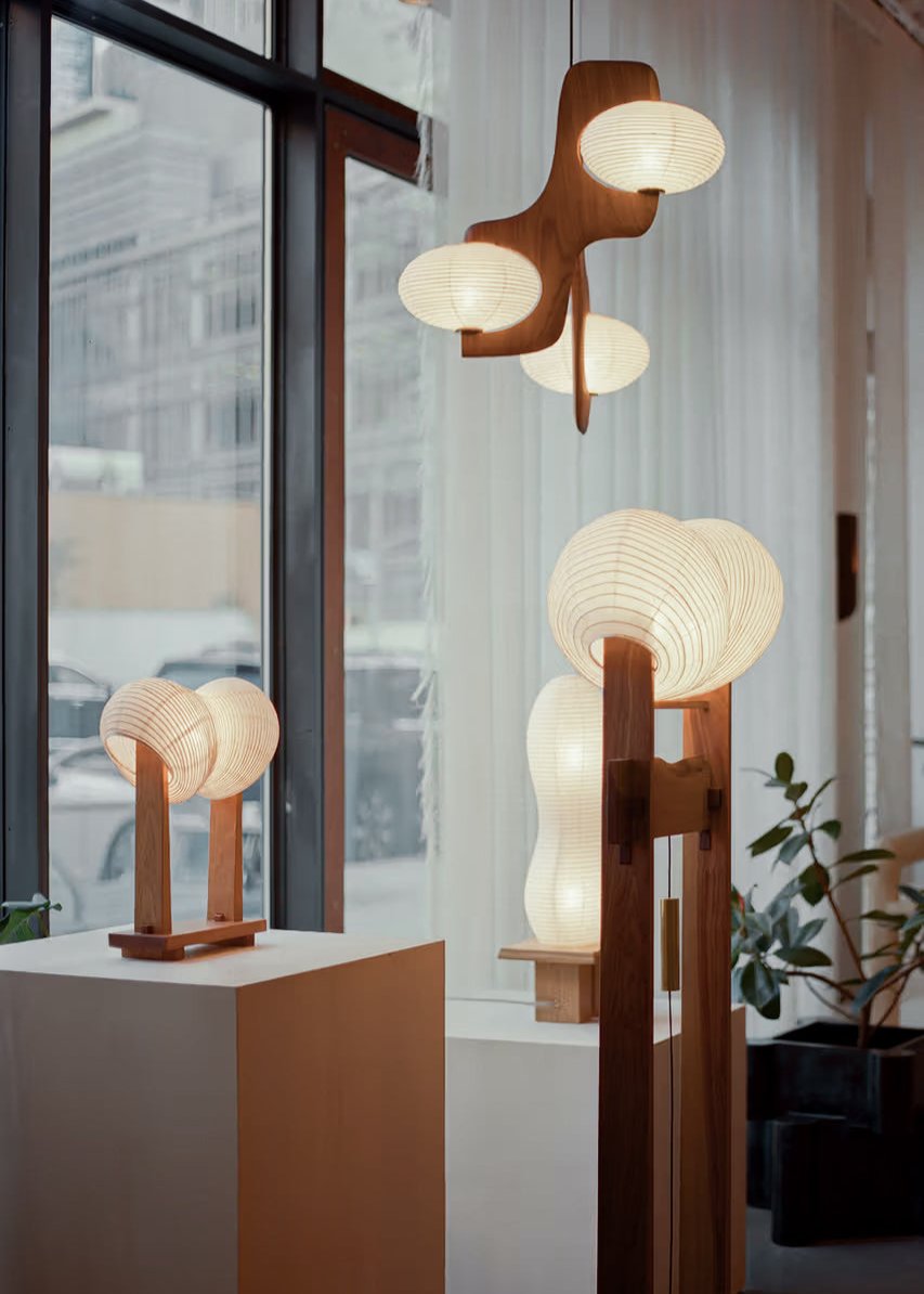 A collection of paper-based lighting by Kawabi composed of a pendant, a floor lamp, and a table lamp displayed within a New York gallery