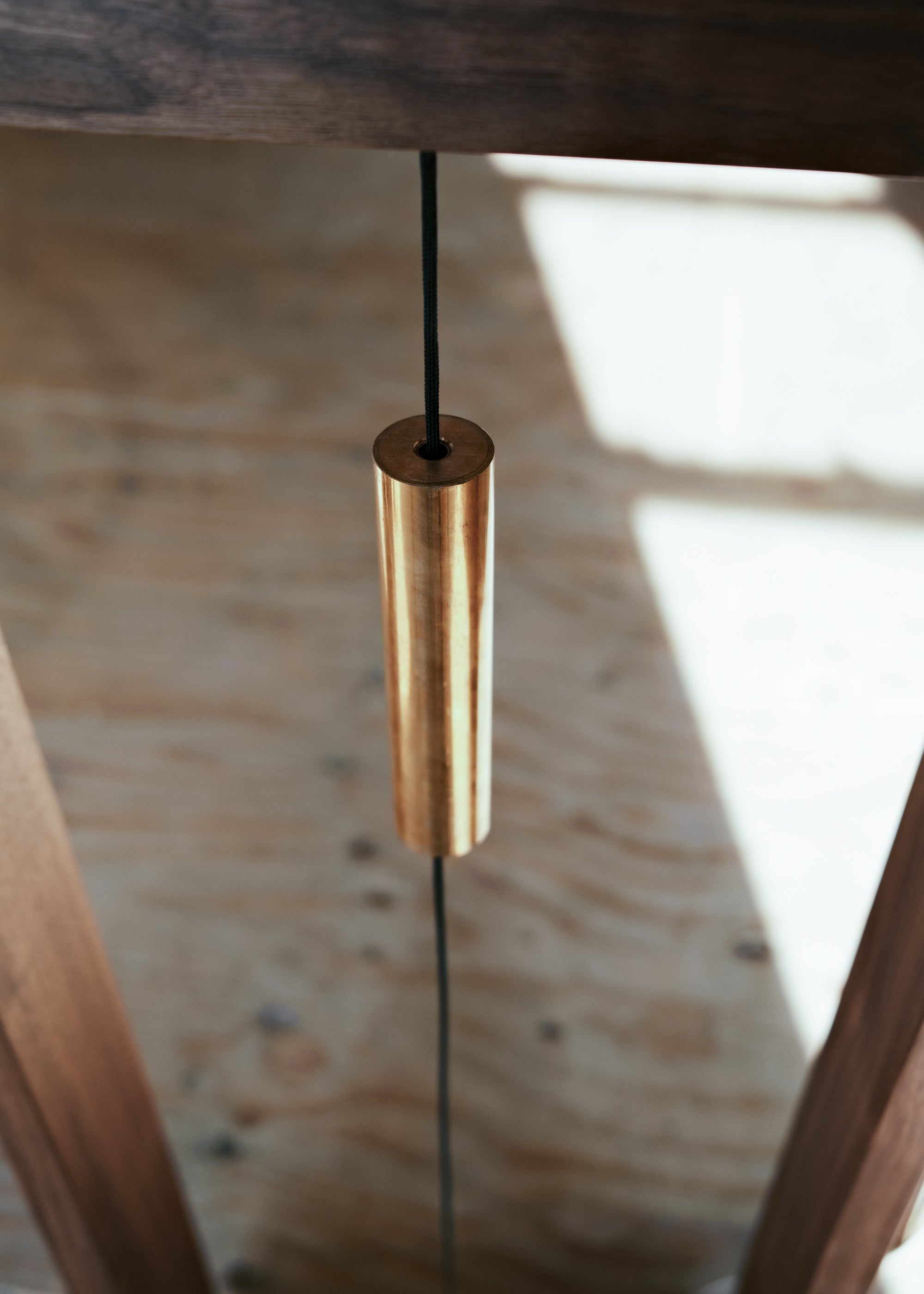 A close-up side view of Kawabi's Souvenir Floor Lamp brass touch switch, a long floating cylinder resembling a windchime