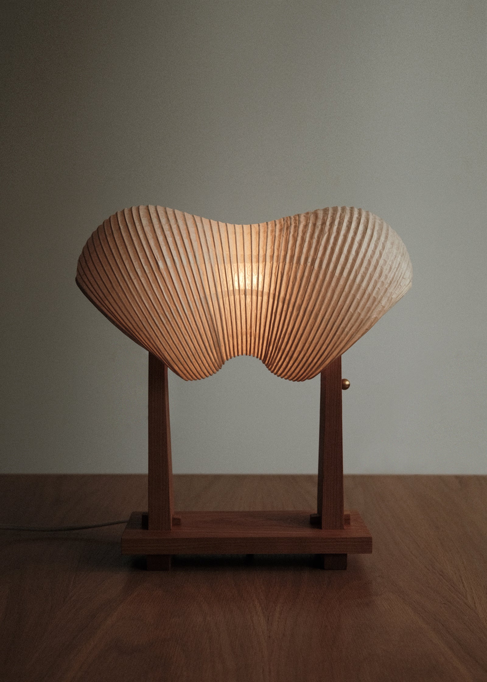 A straight-on shot of Kawabi's Souvenir Table Lamp made of Japanese washi and American Cherry, gently glowing in a dim space.